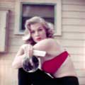 Anita Ekberg is photographed by Milton H. Greene outside in LA for Look Magazine in 1954. Annita is faced to the side sitting wearing a red velour bra and black leggings holding a comb and mirror looking lovely towards the camera.