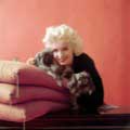 While on an editorial shoot for Look Magazine in 1955, Milton H. Greene took this classic shot of Marilyn Monroe with two Pekingese dogs. Marilyn has her head nestled next to a dog laying on a stack of red pillows as she smiles directly into the camera.