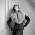 Black and white retro fashion photograph of Sophie Litvak is taken in 1952 by Milton H. Greene for Life Magazine in Paris. Sophie Litvak is wearing an all black assemble with a large fur coat looking downwards and her arms bent with her hands on her sides.